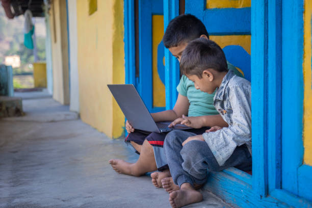 Asian Indian rural kids learning together on laptop while sitting on doorway, e-learning concept , study from home