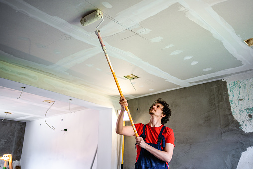 Construction worker painting apartment ceiling with paint roller