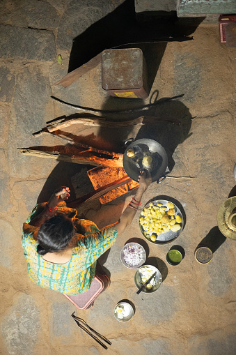 Rural Woman cooking food at night in the courtyard of her house for family using firewood stove