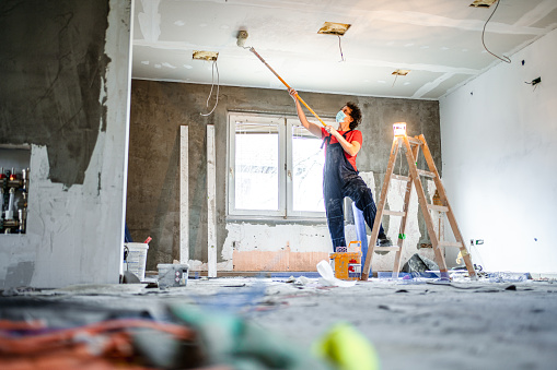 Construction worker painting apartment ceiling with paint roller