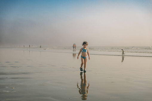 3 year old, multiracial girl walking in the tide of the ocean on a sunny, summer day at the beach.