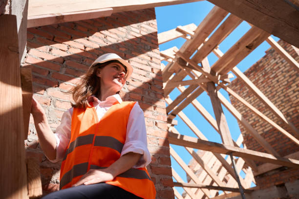 Female construction worker standing on wooden ladder in safety vest and hardhat stock photo