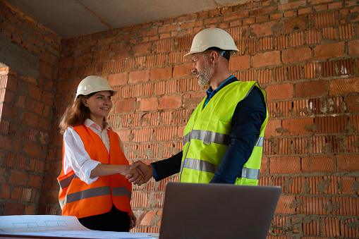 Satisfied with qualitative blueprint foreman shaking hand to female architect in hardhat, meeting on construction site