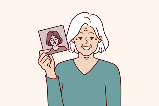 Elderly gray-haired woman shows own old photo for concept of memory of past and nostalgia. Elderly grandmother with smile holds black and white portrait to show what she looked like in youth