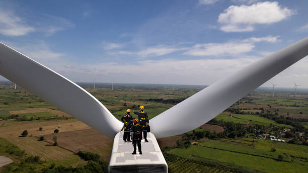 equipo de mantenimiento de turbinas eólicas trabajando en la parte superior de los soportes de turbinas eólicas. grupo de ingenieros técnicos con trajes de seguridad y casco revisando el motor de la turbina eólica en la parte superior de la fuente de a - alternative energy electricity wind turbine team fotografías e imágenes de stock