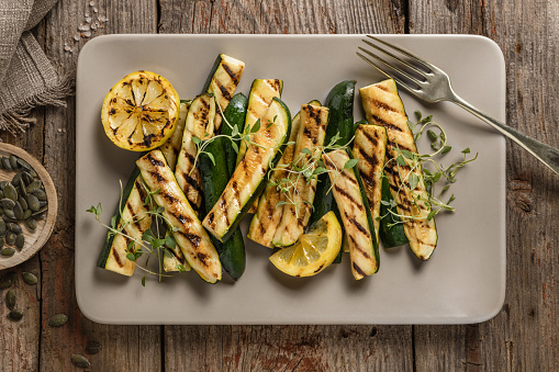 Grilled zucchini and sliced lemon salad topped with fresh herbs and pepita seeds; vegetable appetizer top view on rustic dark wooden table