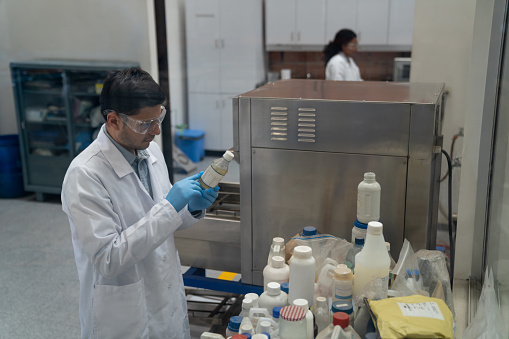 Latin American chemist working at an industrial chemical plant and reading the label on a bottle in the lab