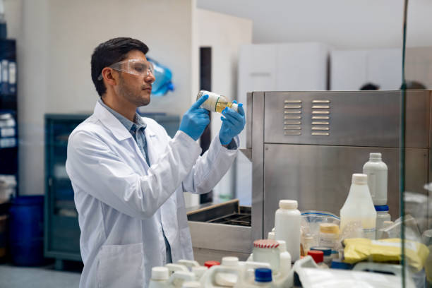 químico trabajando en un laboratorio industrial y mirando un producto químico en una botella - chemical worker fotografías e imágenes de stock