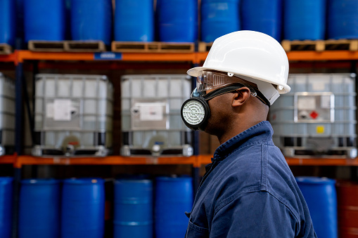 Profile view of an African American chemical plant worker wearing a gas mask and protective workwear at work