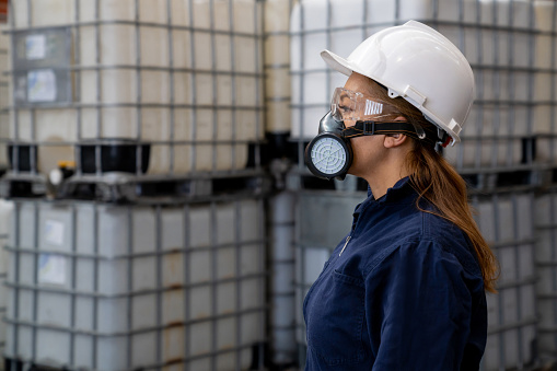 Profile view of a Latin American female chemical plant worker wearing a gas mask and protective workwear at work