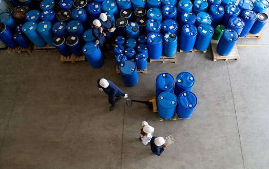 Team of Latin American workers working at a distribution warehouse moving barrels of chemical substances - industrial concepts