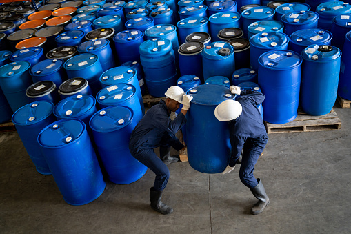 Team of Latin American workers carrying barrels of chemical substances at a distribution warehouse - industrial concepts