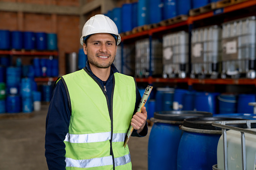 Portrait of a Latin American foreman working at a chemical plant wearing a helmet and holding a clipboard while looking at the camera smiling
