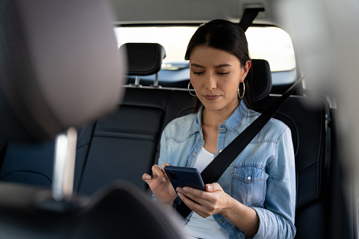 Latin American woman riding a crowdsourced taxi and looking at the route on a mobile app