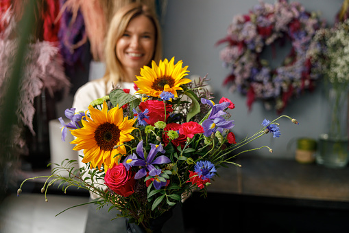 Woman florist smiling and holding beautiful flowers composition in flower shop ready to sale
