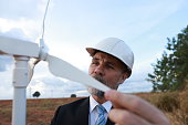 The senior specialist engineer  holding a wind turbine prototype model miniature with windmills in the background