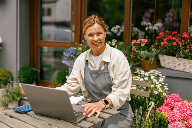 istock Smiling florist working on laptop and taking online orders in store and looking at camera 1502997104