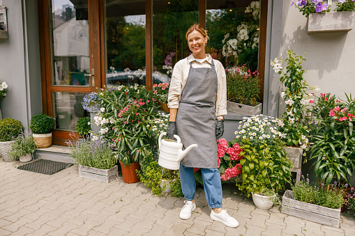 Smiling woman florist taking care of plant watering it in floral shop. Small business concept
