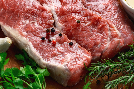 Fresh beef meat on cutting board on dark background with ingredients for cookin, copy space