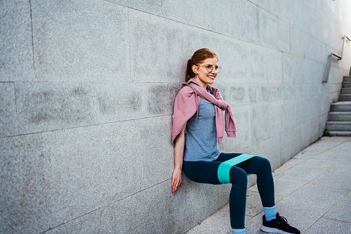 Beautiful young sporty woman doing stretching exercises during her workout in urban environment surrounded with concrete walls. Modern workout concept.