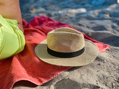 Straw hat on beach towel next to a man with a fluorescent yellow swimsuit