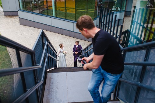 Professional wedding videographer shoots a film with the newlyweds on the stairs