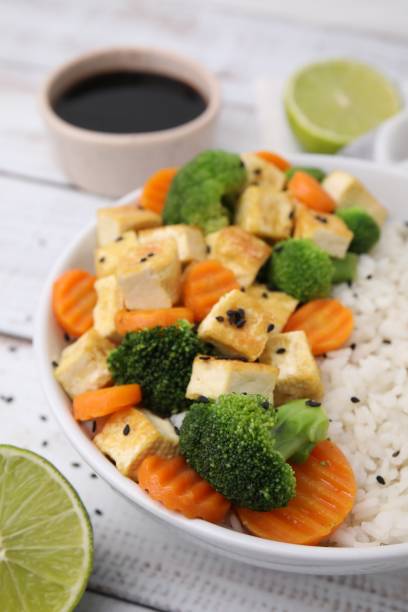 bol de riz avec tofu frit, brocoli et carottes sur table en bois blanc, gros plan - tofu chinese cuisine vegetarian food broccoli photos et images de collection