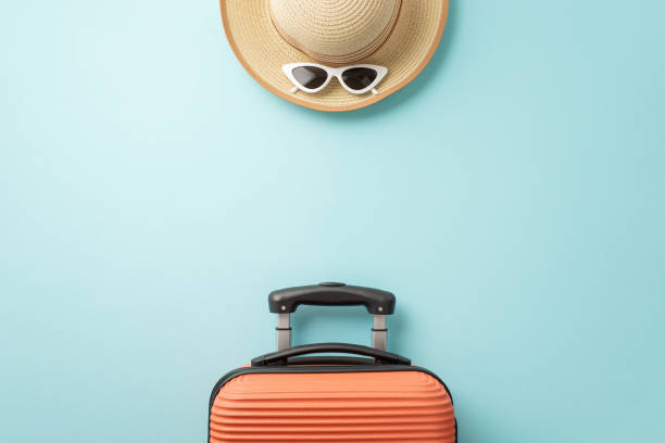 istock Calling all sun seekers! Overhead view of an orange suitcase, beach essentials, sunglasses, and sunhat, on a pastel blue background, featuring blank space for text or advertising 1503016521