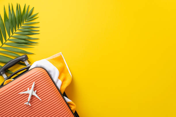 istock Craving ultimate vacation. Top view arrangement with a suitcase, mini airplane, beach necessities, towel, and natural palm leaf on vivid yellow background. Plenty of space for text or advertisements 1503016570