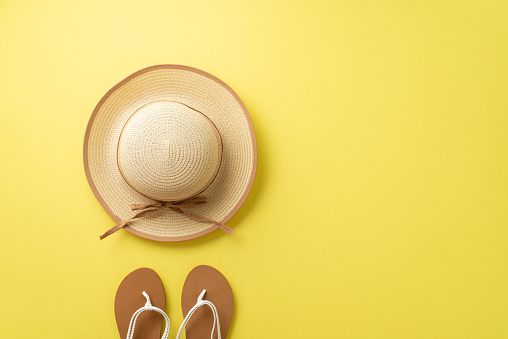 Escape to a sunny paradise. Top view of beach must-haves including sunhat, and sandals against a yellow background with empty space for text or promotions