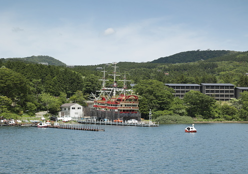 May 27, 2023 - Lake Ashi, Japan: The waterfront of Lake Ashinoko includes a commercial dock, pleasure craft and hotels. A red tour boat undergoes maintenance at the dry dock on the crater lake. Spring afternoon in the Fuji-Hakone-Izu National Park.
