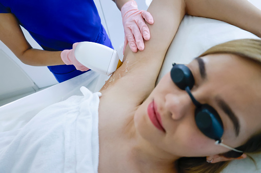 Cosmetologist performing laser hair removal on underarms