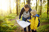 Schoolchild and his mature father hiking together and exploring nature. Little boy with dad looking map during orienteering in forest