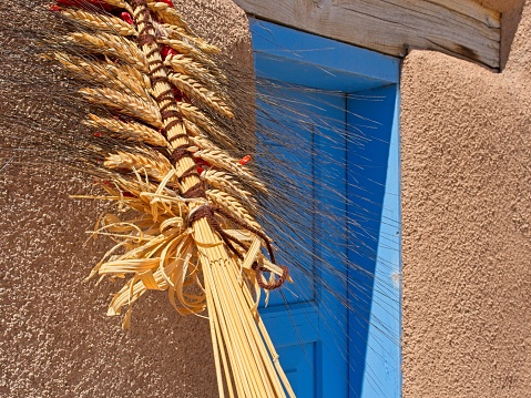 Strung wheat adorning adobe church building and blue window in Ranchos de Taos New Mexico.