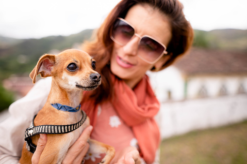 Smiling woman wearing sunglasses sitting with her little chihuahua outdoors during a  break from a walk together