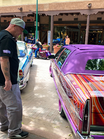 Santa Fe, NM: A man stands near his fancy striped vintage car with a purple roof on the historic Santa Fe Plaza on the annual (June) Lowrider Day.