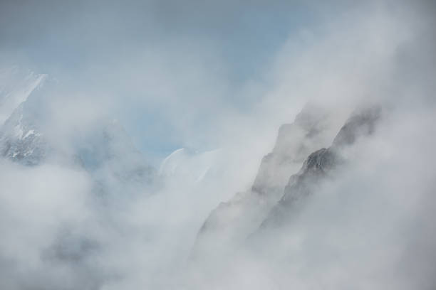 istock Lovely scenery with big snowy mountains in thick clouds. High mountain wall in gantly cloudy sky. Scenic view to large snow mountain in clearance of dense fog. Beautiful diagonal rocks in low clouds. 1503060196
