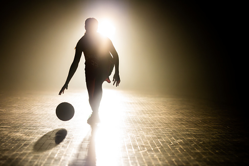 Female basketball player silhouette training at dark indoor court illuminated with lights wide shot