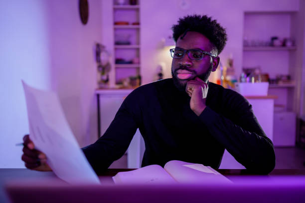 istock A serious self-employed man is sitting at home late at night and working on paperwork in a purple lighted room. 1503060778