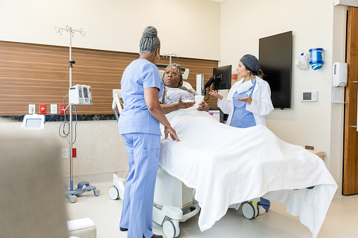 The mature adult female patient on the gurney has an angry discussion with the mid adult female emergency room doctor and the senior adult female nurse.