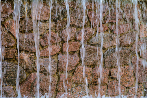 Artificial waterfall with fast falling water jets. Wall made of stacked granite stone.