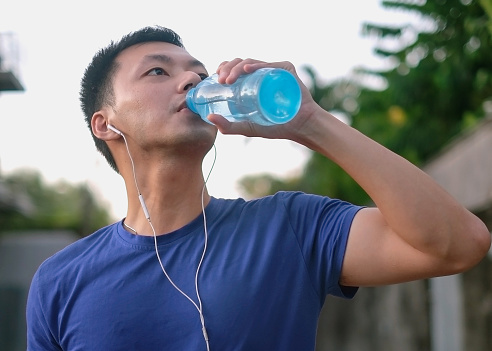 Close-up shot of young Asian man drinking mineral water from plastic bottle