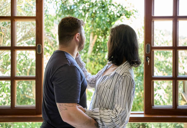 istock Young couple standing by window and looking outside at home 1503111237