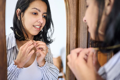 Reflection of beautiful young woman wearing golden necklace looking into mirror at home