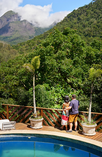 High angle view of a young couple looking at the scenic view while outside on a poolside deck of their tourist resort