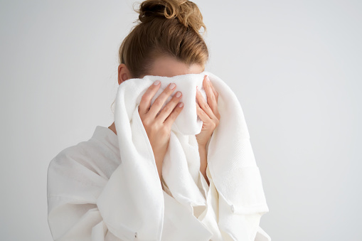 The girl wipes her face with a white terry towel.