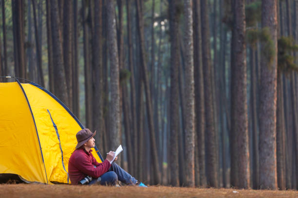 Solo overnight camping while sitting beside tent at campsite in pine forest while writing journal for freedom, solitude, peacefully relaxation getaway to wilderness and nature healing therapy