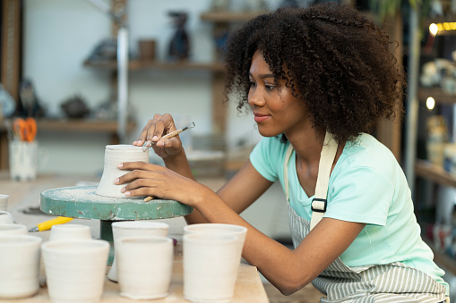 In a tranquil ceramic studio, a talented girl meticulously sculpts and crafts elegant clay pieces, blending artistry and craftsmanship into one.