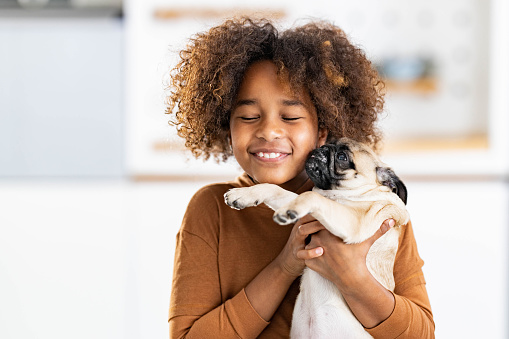 Happy African American girl spending time with her pug at home.