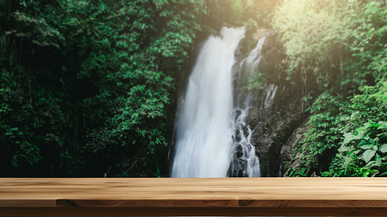 Empty wooden table with the natural background of tropical forest and waterfall. can be used to display or montage products or food